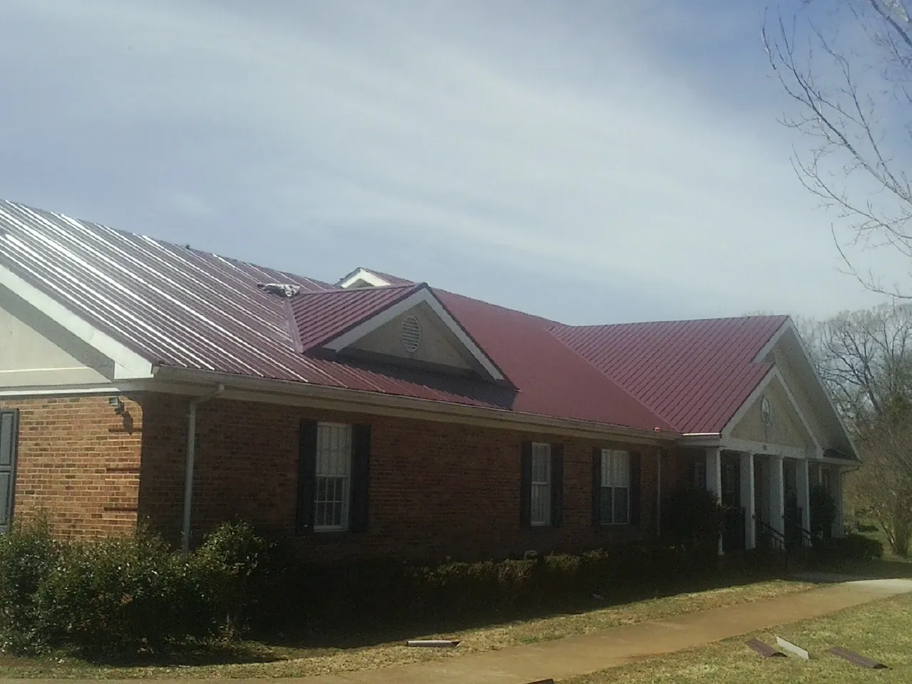 Red metal roof with gabled entries on a long brick building, from a Hail Damage Roof Repair job in Plumtree