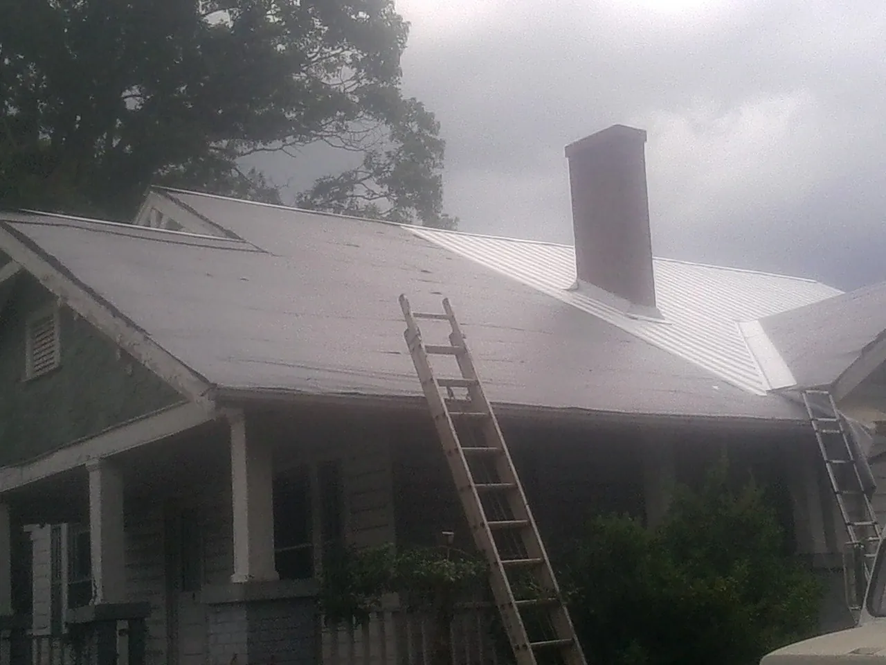 Ladders against a metal roof on an older home with a brick chimney in Plumtree