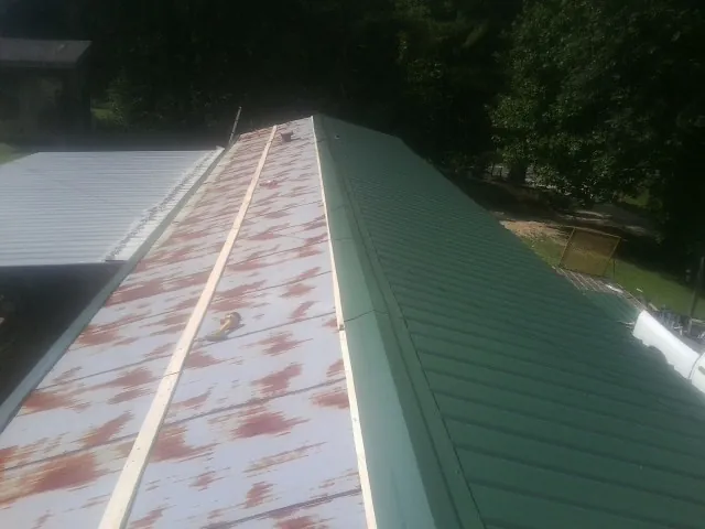 Old rusted panels beside newly installed green metal roofing — Wind Damage Roof Repair by Roofing Brothers in Plumtree