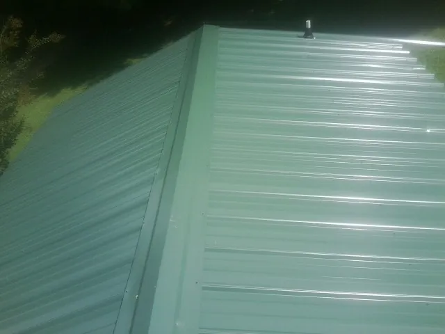 New green metal panels meeting at the ridge of a roof — Flat Roof Repair work by our crew in Plumtree