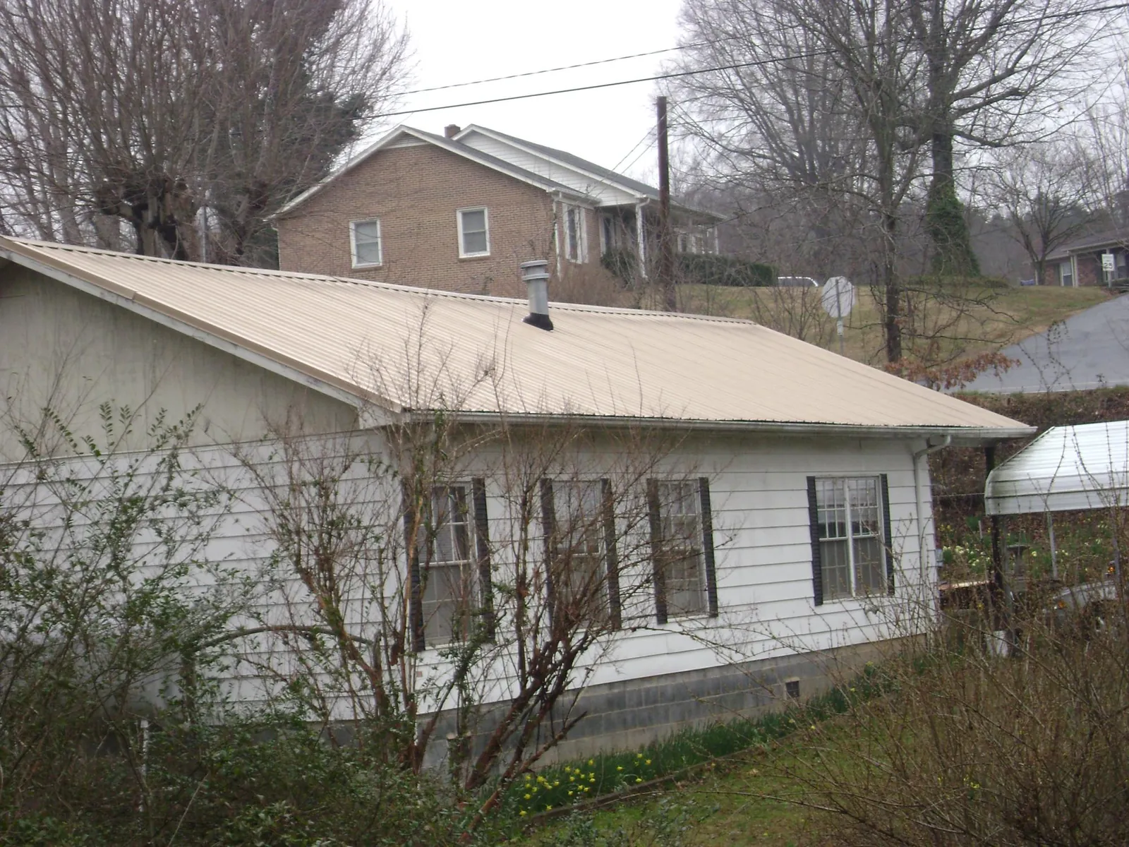 Tan metal roof on a white sided house set into a hillside — Commercial Roofing by Roofing Brothers in Plumtree